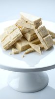 Stacked and scattered white chocolate bars with speckled texture displayed on white pedestal cake stand, ideal for confectionery, dessert, and food styling projects.