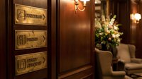 Luxury hotel interior with brass directional signs for concierge, dining and guest services mounted on rich wood paneling in elegant lobby.