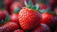 Fresh ripe strawberry macro shot showing detailed texture and seeds on vibrant red fruit with natural green leaves and blurred background. For food industry.