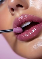 Close-up of glossy mauve lips with liquid lipstick applicator brush showing professional makeup application technique on light brown skin with dewy finish.