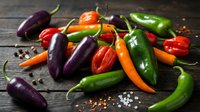Colorful mix of fresh hot chili peppers in red, green, orange, and purple on a rustic dark wooden table with scattered spices.