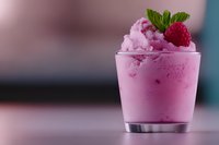 Pink raspberry ice cream dessert topped with fresh mint leaf and berry in glass cup against blurred background. Creamy frozen treat for summer menu.