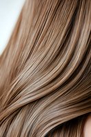 Close-up of smooth, shiny light brown hair strands flowing in gentle waves, showcasing healthy texture for beauty and haircare concepts.