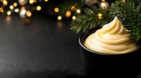 Creamy soft serve vanilla ice cream swirl in black bowl against dark background with bokeh lights and pine branches, festive winter dessert setting.
