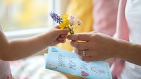 Young woman receiving small wildflower bouquet with grape hyacinth and yellow blooms as Mother's Day gift with handmade card near bright window.