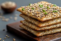 Crispy crackers with sesame seeds and pumpkin seeds stacked on wooden board, close up view of healthy snack with whole grain and seeds garnish.