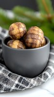 Roasted chestnuts in gray ceramic bowl on checkered napkin, selective focus with blurred background. Fresh seasonal nuts with cracked shell surface.