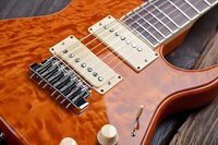 Close-up of an amber electric guitar body with quilted maple top, chrome hardware, dual pickups, and strings on a wooden surface.
