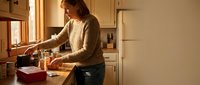 Young woman preparing healthy breakfast in modern kitchen with natural sunlight streaming through window creating warm cozy morning atmosphere.