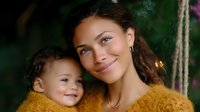 Young mixed race mother and toddler child sharing tender moment on garden swing, wearing matching yellow sweaters against green natural background.