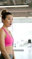Woman in pink sports bra with surprised expression during workout at gym. Fitness enthusiast, East Asian appearance, mid-thirties, athletic build, hair in bun, indoor training facility setting.