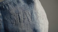 Stay safe embroidered text on blue denim fabric, close-up texture shot with soft focus background for fashion and lifestyle use.