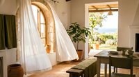 Bright Mediterranean interior with flowing white curtains, wooden arched window, potted plant, and desk workspace with natural sunlight for home design and lifestyle projects.