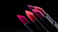 Pink and red lipsticks arranged in diagonal line on black background, dramatic lighting creates glossy reflection on cosmetic products for beauty and makeup.