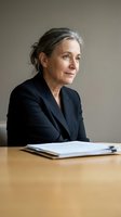 Mature businesswoman with gray hair sitting at desk with documents in modern office environment for corporate and professional presentations.
