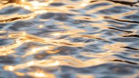 Golden sunlight reflects on gentle rippling water surface creating abstract pattern of light and shadows in tranquil natural setting at sunset.