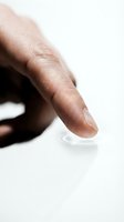 Close-up of a dark-skinned hand fingertip pressing a soft contact lens on a white surface, highlighting eye care and vision correction concepts.
