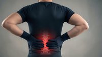 Man in dark shirt touching lower back with glowing red pain indication showing lumbar spine discomfort and muscle tension for medical concept.