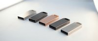 Five metallic USB flash drives arranged in a row on white surface, featuring sleek designs in silver, black, rose gold, and gunmetal finishes for data storage and file transfer needs.