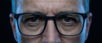 Middle-aged Caucasian male wearing black-framed eyeglasses, looking directly at camera with serious expression against dark background. Professional headshot suitable for corporate, business, and editorial use.
