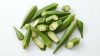 Fresh green okra pods whole and sliced showing seeds, healthy organic vegetable ingredient for cooking and nutrition on white background.