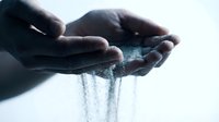 Close-up of hands holding and pouring water, showing droplets flowing through fingers against light background for hydration and wellness concepts.