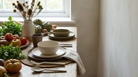 Rustic kitchen table setting with ceramic dinnerware, fresh vegetables, herbs and natural dried flowers creating cozy farmhouse dining atmosphere.