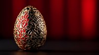 Decorative golden egg with intricate floral pattern on red and black background. Ornate metalwork design features delicate swirls and botanical elements.