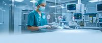 Male surgeon in green scrubs and surgical mask working with digital holographic interface in modern operating room with advanced medical technology equipment.