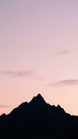 Silhouetted mountain peak against soft pink and purple twilight sky with wispy clouds during sunset or sunrise, creating a serene landscape for nature and travel designs.
