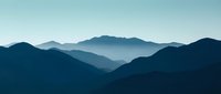 Layered mountain silhouettes in deep blue and teal tones create atmospheric depth, suitable for backgrounds, wallpapers, and nature-themed design projects.