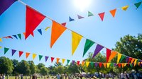 Colorful triangular bunting flags hanging outdoors against blue sky and green trees creating festive party atmosphere for celebrations and events.