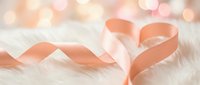 Elegant coral pink satin ribbon forming heart shape on soft white fur background with warm bokeh lights for romantic Valentine's Day celebrations.