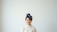 Young Asian male child wearing cream-colored turtleneck sweater with dark hair styled upward, smiling at camera against neutral white background for portrait use.