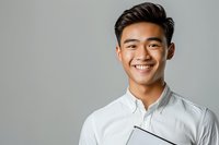 Young Asian male professional with bright smile wearing white button-up shirt holding digital tablet, perfect for business, education, or corporate marketing materials against neutral gray background.