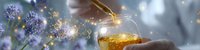 Pouring golden honey with magical sparkles and lavender flowers in dreamy atmosphere. Glowing particles create ethereal mood against blurred purple background.