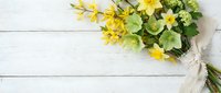 Fresh yellow wildflower bouquet with green foliage tied with natural twine on white wooden background. Spring floral arrangement for greeting cards.