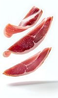 Thin slices of cured prosciutto ham floating in air on white background, showing marbled texture and rich red color. Isolated food photography for culinary use.