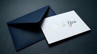 Elegant thank you card with silver script lettering leaning against a navy blue envelope on dark background, perfect for gratitude messaging.