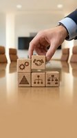 Businessman hand placing wooden blocks with business icons representing teamwork, leadership and corporate strategy in modern office environment.