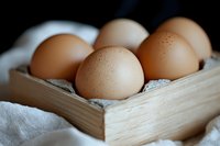 Fresh brown eggs in rustic wooden box on white linen cloth. Natural organic food composition with soft selective focus and dark background.