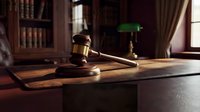 Wooden judge gavel on desk in traditional law office with books and green banker lamp creating professional legal atmosphere for justice concepts.