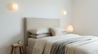 Modern minimalist bedroom interior with beige headboard, neutral bedding, warm pendant lights and wooden stool creating cozy scandinavian atmosphere.