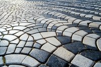 Curved pattern of gray and black cobblestone pavement creating geometric shapes and perspective lines, suitable for architectural and urban design backgrounds.