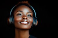 Young African American woman with bright smile wearing wireless headphones against dark background, radiating joy and positive energy in dramatic lighting.