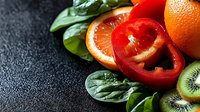 Sliced red bell pepper and kiwi fruit with fresh spinach leaves arranged on dark textured surface for food styling and culinary design projects.