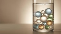 Decorative glass beads and spheres submerged in clear water inside a transparent cylinder, creating an artistic still life composition for home decor and design projects.
