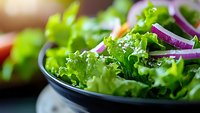 Fresh green lettuce salad with purple onion rings in dark bowl, macro food photography with selective focus and bokeh background.