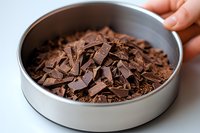 Dark chocolate shavings and flakes in round metal container, close up view showing texture and layers of gourmet cooking chocolate pieces.