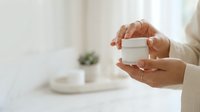 Middle-aged woman with medium skin tone holding white cosmetic jar, showcasing skincare product packaging for beauty, wellness, and dermatology marketing campaigns.